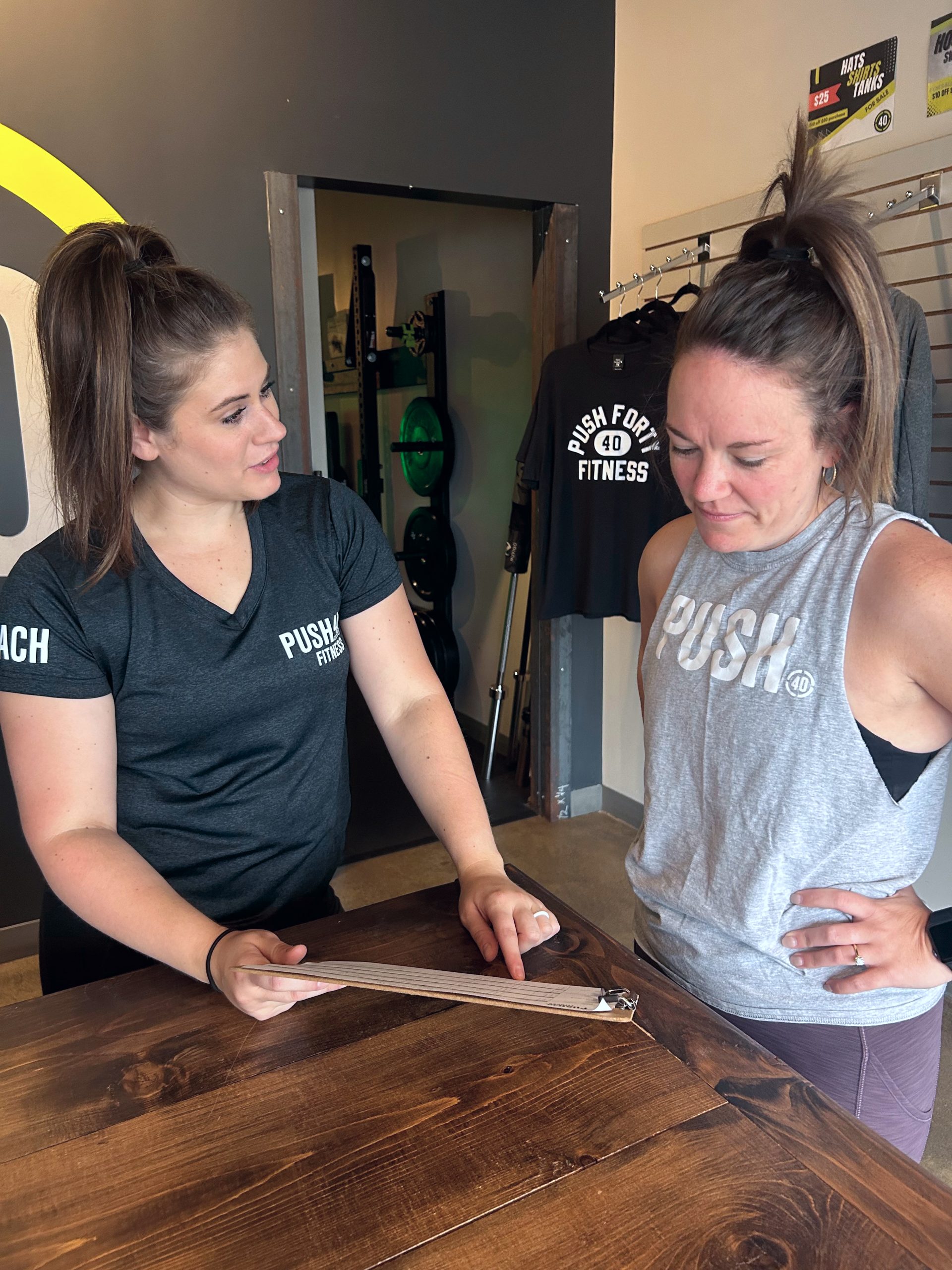 Coach Maura consulting with a member at the front desk of Push 40 Fitness.